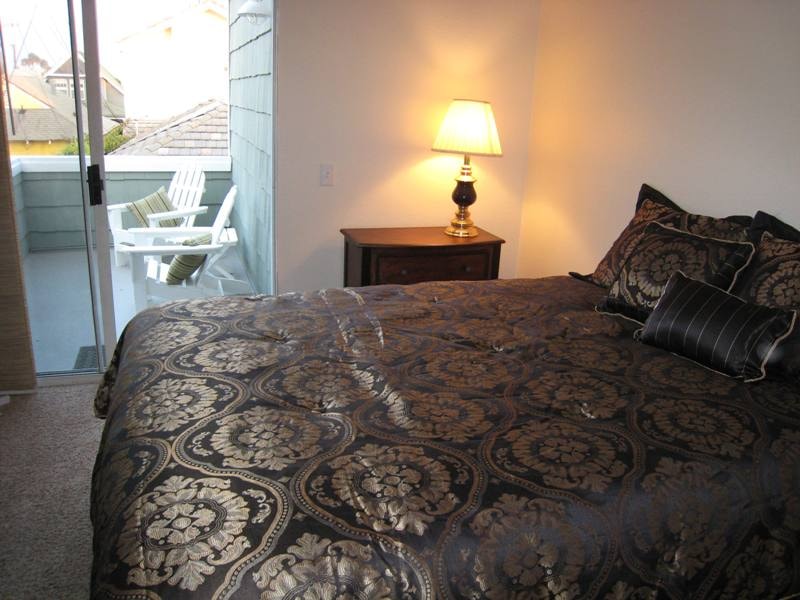 Lower unit primary bedroom with queen bed, ornate bedding, and balcony access