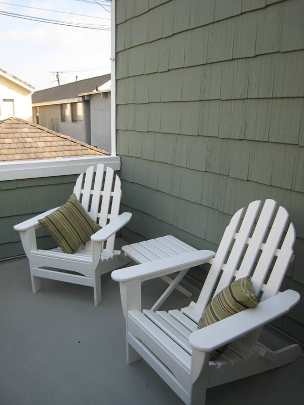 Lower unit primary bedroom rear balcony with white Adirondack chairs and side table