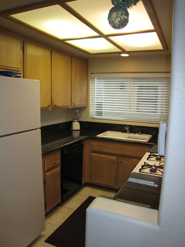 Lower unit kitchen with gas range, microwave, black countertops, and wood cabinetry