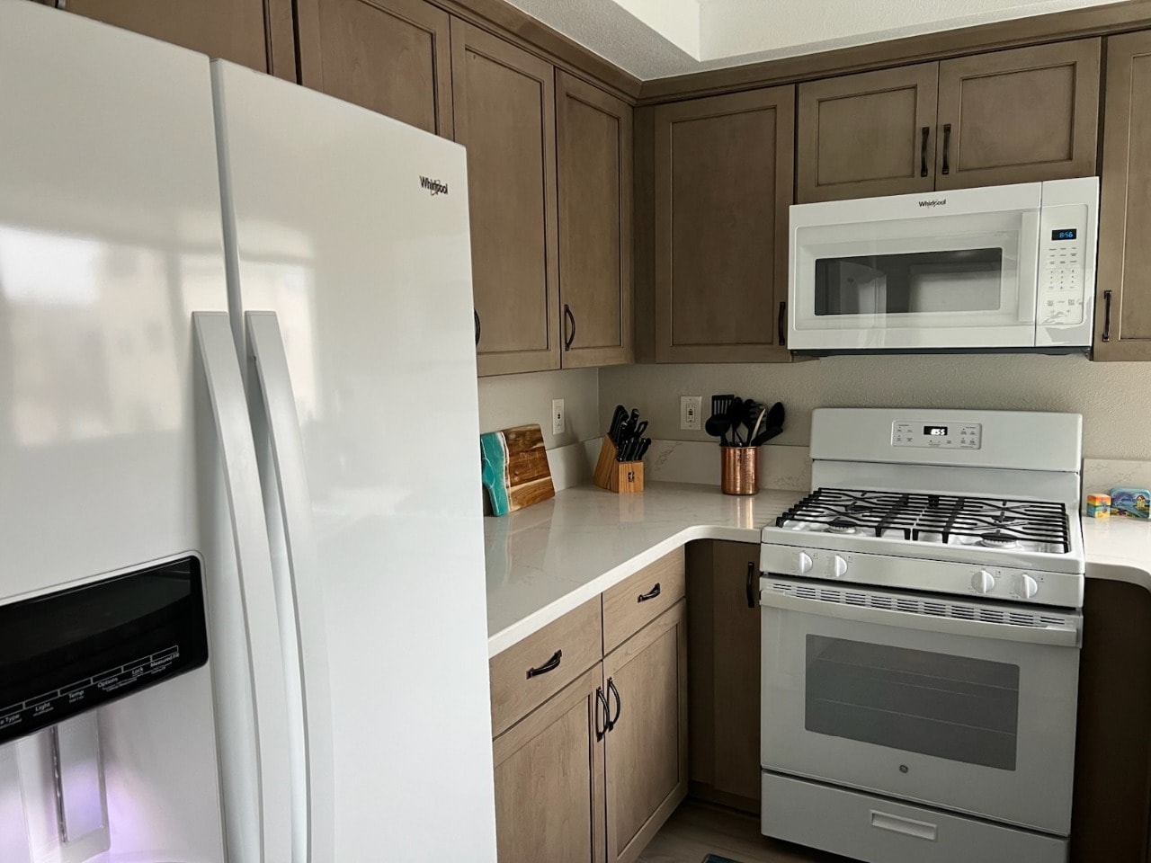 Upper unit kitchen with Whirlpool refrigerator, gas range, and wood cabinetry